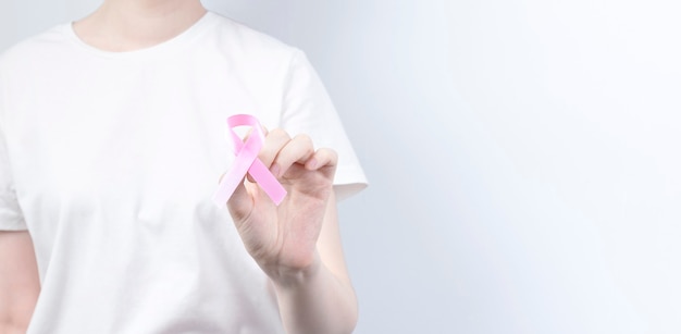 Concept de la journée mondiale du cancer du sein. Une femme en T-shirt blanc tient un ruban rose dans sa main. Octobre Mois de la sensibilisation au cancer du sein. Espace de copie