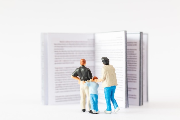 Concept de la Journée mondiale du livre Personnes miniatures Famille heureuse lisant un livre sur un fond blanc