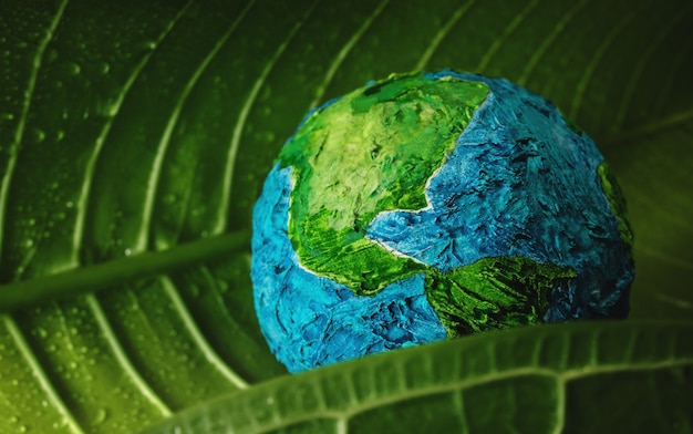 Concept de la journée mondiale de la terre. Feuille verte d'humidité avec l'eau de gouttelette embrassant un globe fait main Environnement à aimer et à soigner