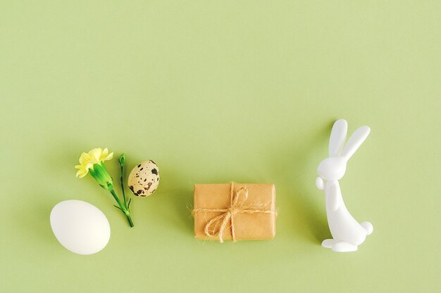 Concept de Joyeuses Pâques. Divers oeufs, fleurs, cadeau d'artisanat et figurine de lapin sur fond vert avec espace de copie