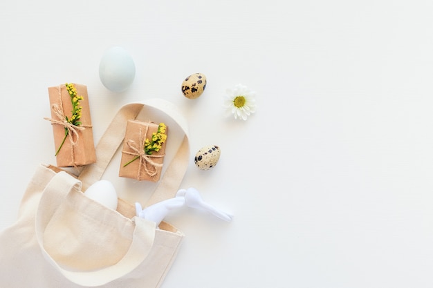 Concept de Joyeuses Pâques. Oeufs, fleurs jaunes, cadeau artisanal et figurine de lapin s'envolent d'un sac textile sur fond blanc