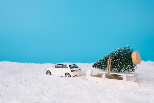 Concept De Joyeux Noël. La Photo En Gros Plan D'une Voiture Miniature Jouet S'éloignant Avec Un Arbre Jouet Dans La Neige