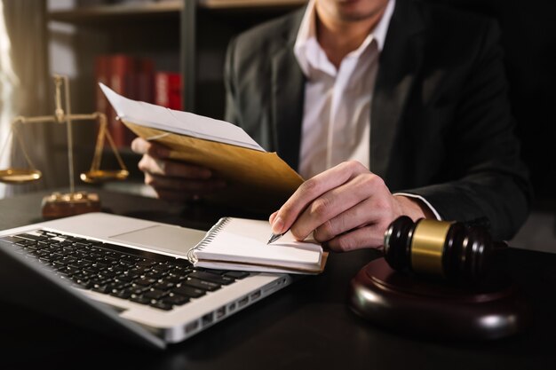 Concept de justice et de droit. Juge masculin dans une salle d'audience avec le marteau, travaillant avec, ordinateur et clavier d'amarrage, lunettes, sur table à la lumière du matin