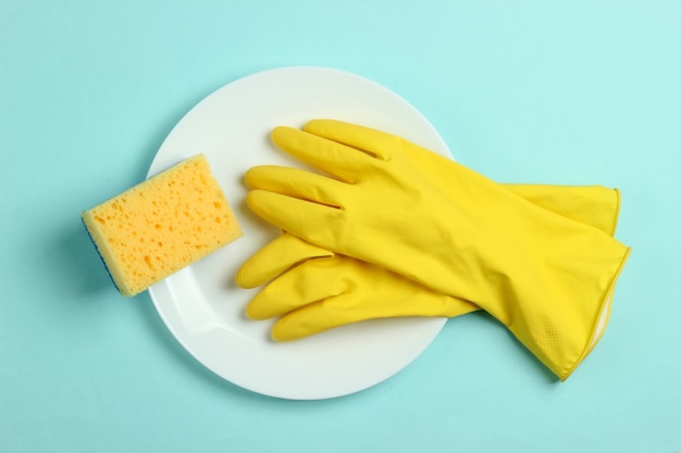 Concept de lavage de vaisselle. Assiette avec une éponge et des gants en caoutchouc sur fond bleu pastel. Vue de dessus