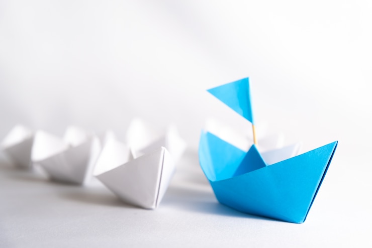 Photo concept de leadership. navire de papier bleu avec le drapeau du plomb parmi les blancs.