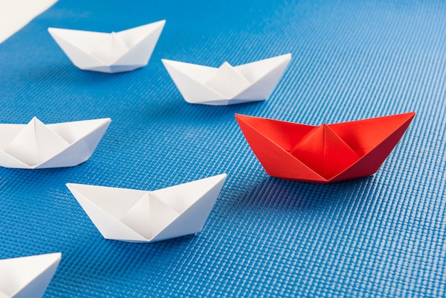 Concept de leadership avec navire de papier rouge menant parmi fond blanc et bleu