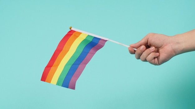 Concept LGBT. La main tient un drapeau arc-en-ciel sur fond vert menthe ou bleu tiffany.