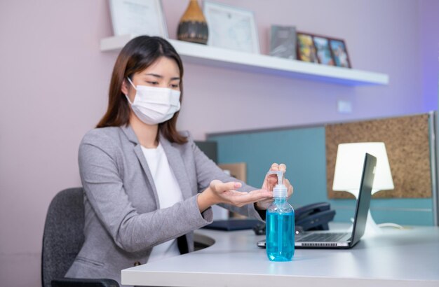 Concept de lieu de travail de sécurité Jeune femme d'affaires portant un masque facial et utilisant du gel pour les mains Sanitizer