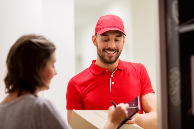 concept de livraison, de courrier, de personnes et d'expédition - homme heureux livrant une boîte à colis et signature du client sur un ordinateur tablette à la maison