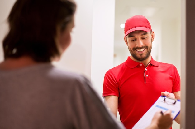 concept de livraison, de courrier, de personnes et d'expédition - homme heureux avec presse-papiers et formulaire de signature du client à la maison