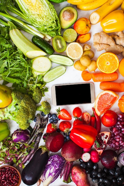 Concept de livraison de fruits et légumes biologiques frais de la ferme. Produits de la ferme, smartphone avec nourriture végétalienne arc-en-ciel, vue de dessus
