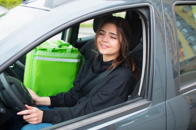 Concept de livraison de nourriture. La livreuse a un sac à dos frigo vert. Elle est assise dans une voiture et livre de la nourriture aux clients