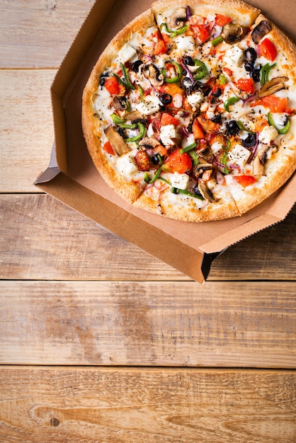 Concept de livraison. Pizza aux légumes dans une boîte en carton ouverte sur table en bois, espace copie, vertical