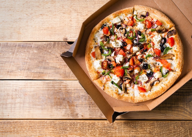 Concept de livraison. Pizza aux légumes dans une boîte en carton ouverte sur table en bois, espace copie