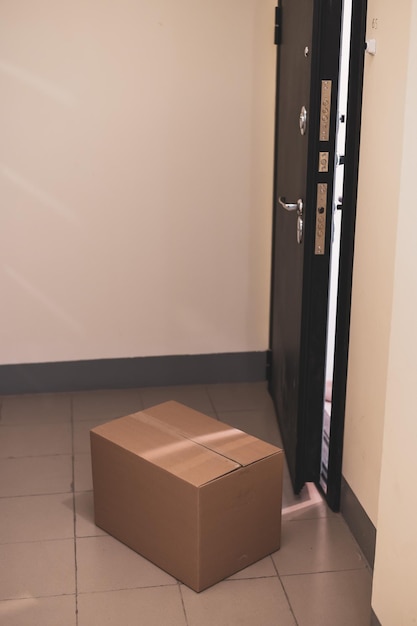 Le concept de livraison de porte sans contact pendant la période de quarantaine Boîte en carton avec achat en ligne à la porte d'entrée ouverte dans un hall vide en cas de danger de coronavirus