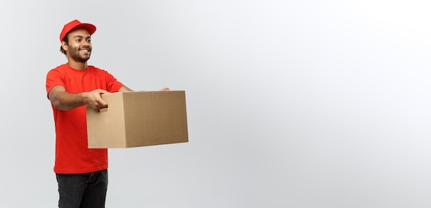 Photo concept de livraison portrait d'un livreur afro-américain heureux en tissu rouge tenant un paquet de boîte isolé sur fond de studio gris espace de copie