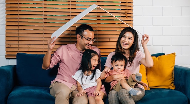 Le concept de logement et de déménagement prend forme avec une famille heureuse mère père et enfants tenant un toit en carton sur le canapé