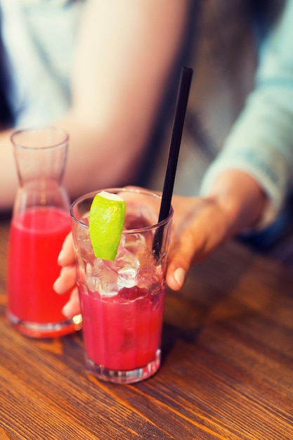 concept loisirs, boissons, personnes et vacances - gros plan sur une main de femme tenant un verre de jus de fruits ou un cocktail avec de la paille et de la glace