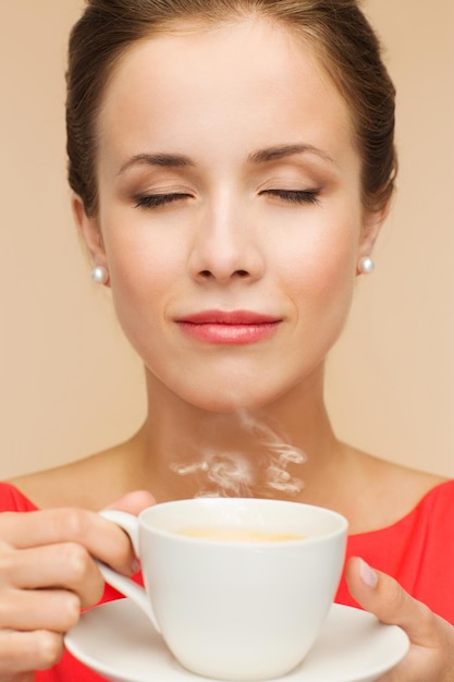 concept de loisirs, de bonheur et de boisson - femme souriante en robe rouge avec une tasse de café