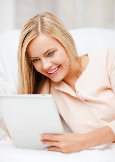 concept de loisirs et d'éducation - femme souriante allongée sur le canapé avec tablet pc