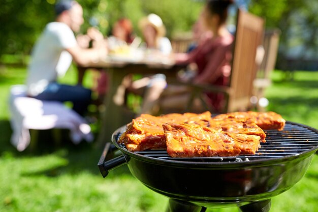 concept de loisirs, de nourriture, de personnes et de vacances - cuisson de la viande sur un barbecue à la fête d'été