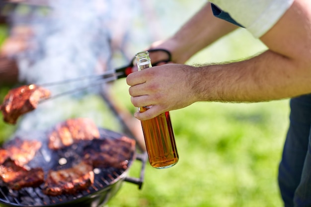 concept de loisirs, de nourriture, de personnes et de vacances - homme cuisinant de la viande sur un barbecue lors d'une fête d'été en plein air