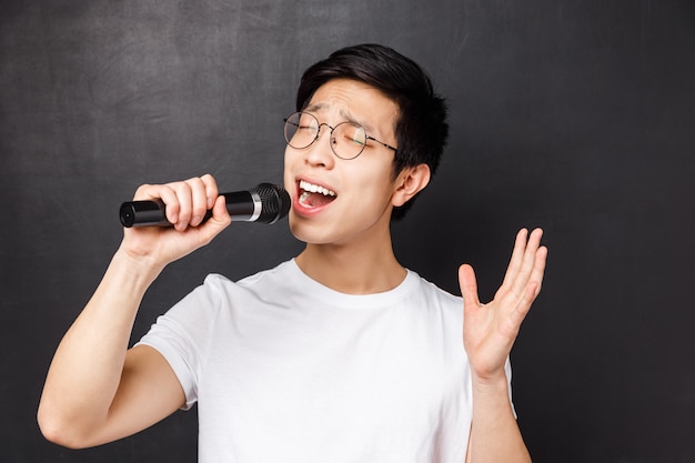 Concept de loisirs, de personnes et de musique. Portrait en gros plan d'un mec asiatique passionné et insouciant aime chanter des chansons, tenir le microphone et lever la main, jouer devant des amis lors d'une soirée karaoké