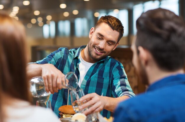 concept de loisirs, de personnes et de vacances - homme souriant avec des amis versant de l'eau de la cruche au restaurant