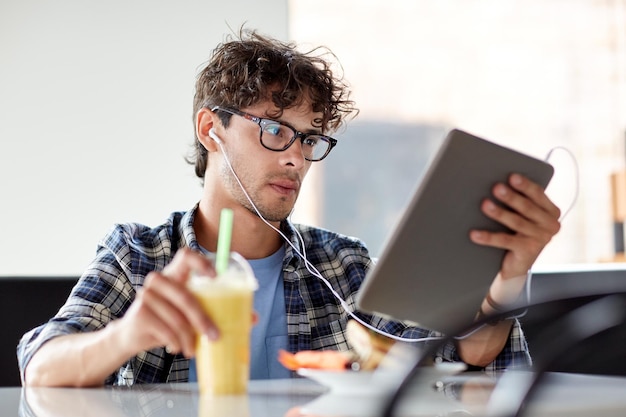 concept de loisirs, de technologie, de communication et de personnes - homme créatif avec ordinateur tablette et écouteurs écoutant de la musique et buvant un shake à la table du café