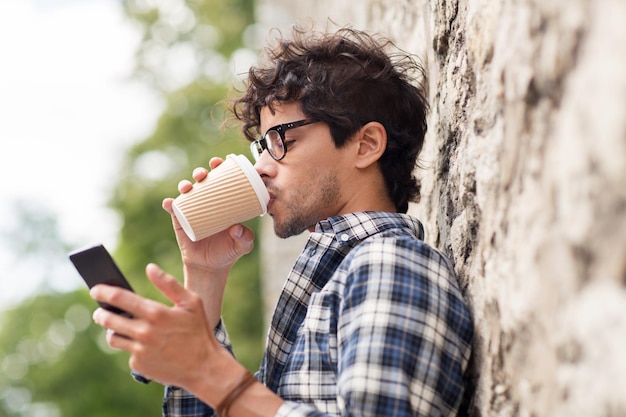 concept de loisirs, de technologie, de communication et de personnes - homme avec un smartphone buvant du café à partir d'une tasse de papier jetable et d'un message texte dans la rue de la ville