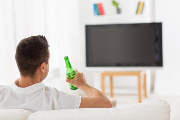 concept de loisirs, de technologie, de médias de masse et de personnes - homme regardant la télévision et buvant une bouteille de bière à la maison depuis l'arrière
