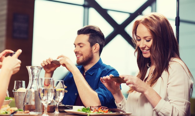 concept de loisirs, de technologie, de style de vie et de personnes - amis heureux avec des smartphones prenant des photos de nourriture au restaurant