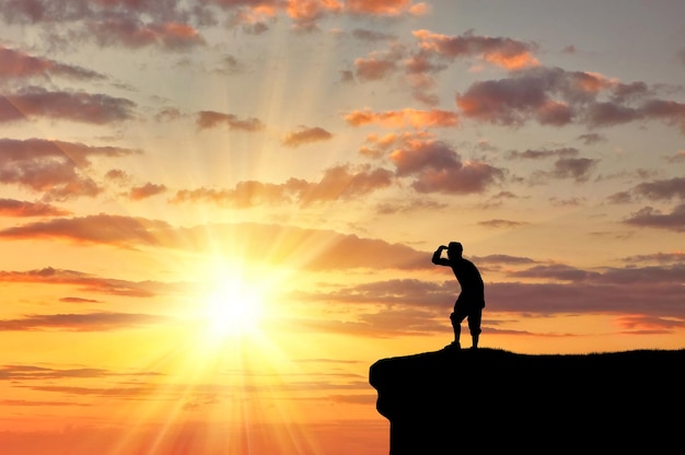 Concept de loisirs et de tourisme. Silhouette d'un homme heureux au sommet de la montagne regardant au loin au coucher du soleil