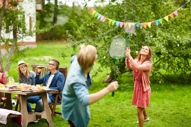 concept loisirs, vacances, personnes et sport - amis heureux jouant au badminton ou au volant lors d'une fête de jardin d'été