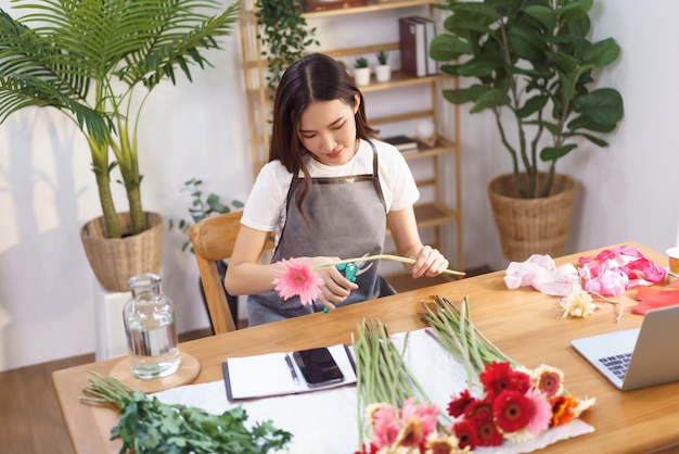 Concept de magasin de fleurs Femme fleuriste coupant gerbera avec des ciseaux pour se préparer à la fabrication de vase à fleurs