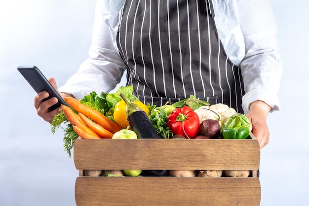 Concept de magasinage de marché biologique à la ferme Boîte en bois avec légumes et fruits crus d'automne d'été dans les mains des femmes agricoles sur fond blanc