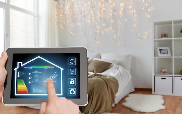 Photo concept de maison intelligente et de technologie en gros plan de mains masculines pointant le doigt vers une tablette pc avec les réglages de la maison à l'écran sur le fond de la chambre à coucher