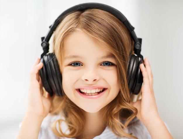 concept de maison, de technologie et de musique - petite fille avec des écouteurs à la maison