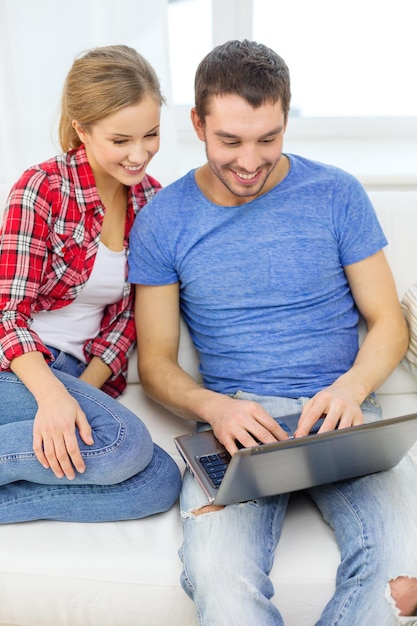 concept de maison, de technologie et de relations - couple souriant avec ordinateur portable à la maison