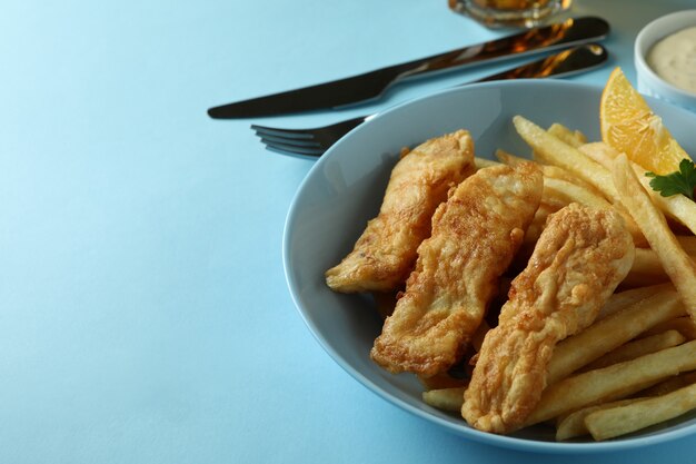 Concept de manger savoureux avec du poisson frit et des frites et de la bière sur bleu