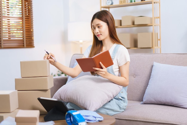 Concept de marchand en ligne Une femme entrepreneur écrit sur une boîte à colis après avoir lu l'adresse sur un ordinateur portable