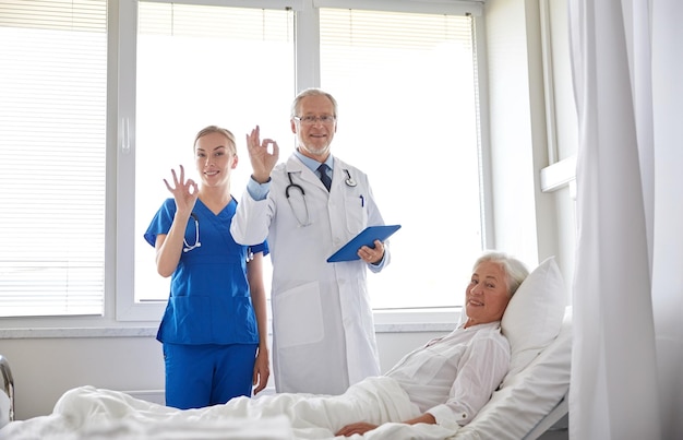 concept de médecine, d'âge, de soins de santé et de personnes - médecin et infirmière avec ordinateur tablette visitant une patiente âgée et montrant un signe ok à l'hôpital