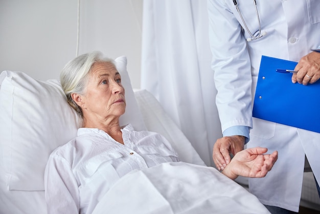 concept de médecine, d'âge, de soins de santé et de personnes - médecin avec presse-papiers visitant une patiente âgée et vérifiant son pouls à l'hôpital