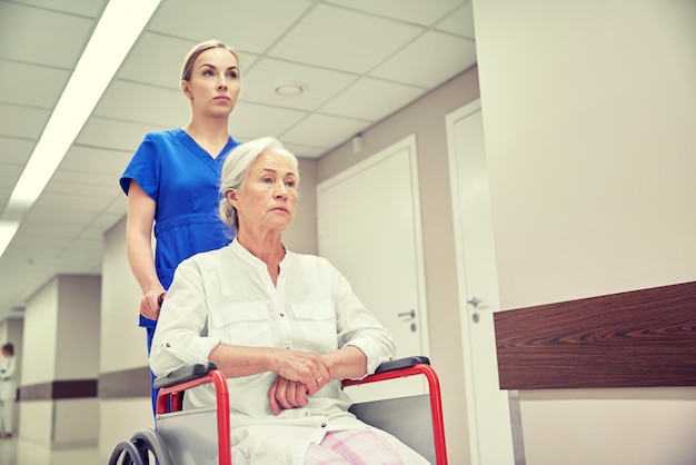 concept de médecine, d'âge, de soutien, de soins de santé et de personnes - infirmière prenant une patiente âgée en fauteuil roulant dans le couloir de l'hôpital