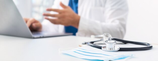 Concept de médecine en ligne. Stéthoscope et masque médical sur le lieu de travail des médecins en arrière-plan. médecin effectue une consultation en ligne des patients à l'aide d'un ordinateur portable