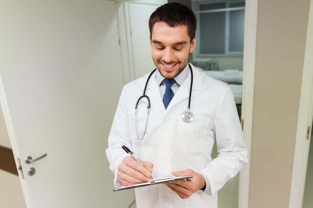 concept de médecine, de soins de santé et de personnes - médecin souriant heureux écrivant dans le presse-papiers à l'hôpital