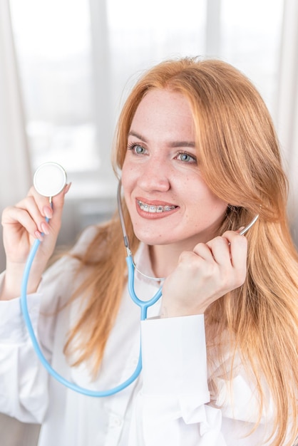 Concept médical Infirmière souriante avec des bretelles et un stéthoscope à la main Femme médecin heureuse et riante dans un manteau blanc posant à la caméra Employé de l'hôpital