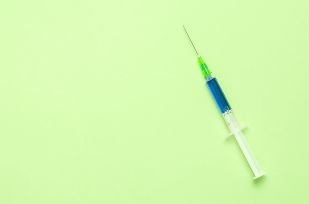Concept médical, injection, vaccination. Seringue avec un liquide bleu sur fond vert. Copier l'espace