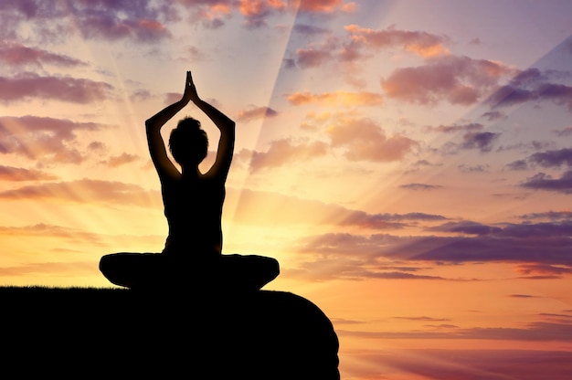 Concept de méditation et de relaxation. Silhouette d'une fille pratiquant l'exercice de yoga sur fond de coucher de soleil