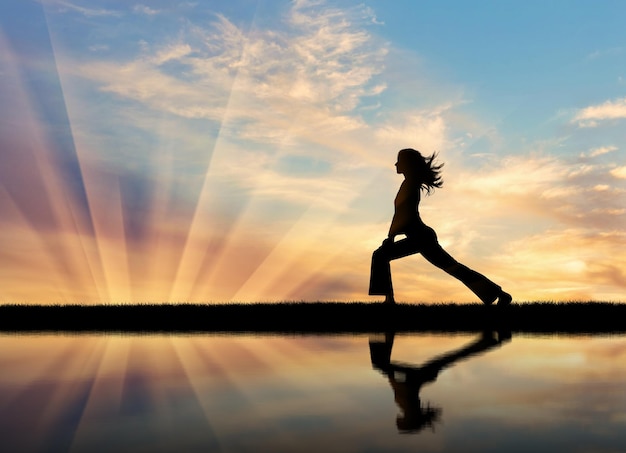 Concept de méditation et de relaxation. Silhouette d'une fille pratiquant le yoga au coucher du soleil et reflet dans l'eau